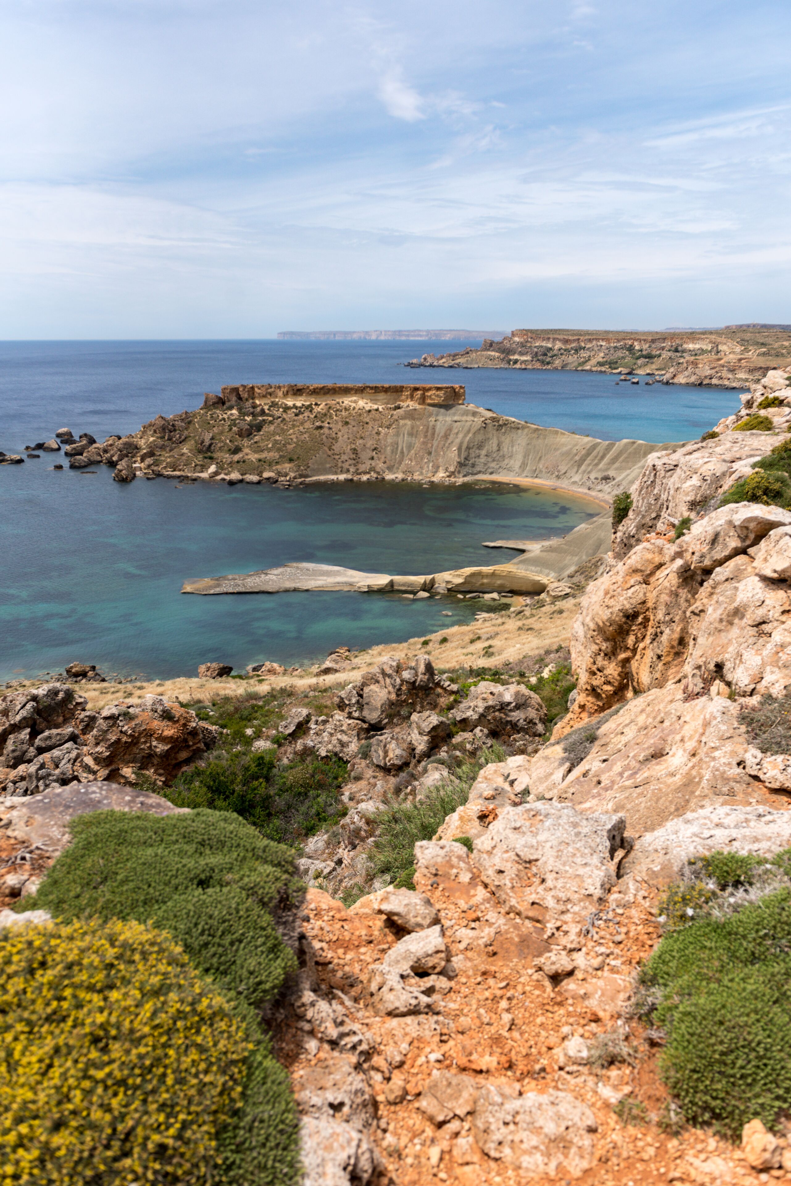 Paesaggio costiero con terreno roccioso e mare blu cristallino.