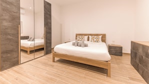 A modern bedroom with a wooden bed, a large mirror, and a wardrobe. - Charming 2BR in Historic Valletta | Prime Central Location (Valletta)
