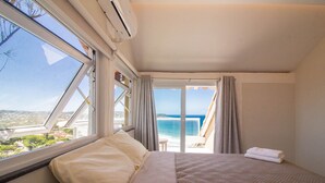 Une chambre avec un grand lit, une fenêtre donnant sur la mer et un balcon avec une table et des chaises.