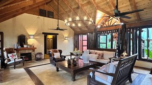 A spacious living room with high ceilings, wooden beams, a fireplace, and large windows.