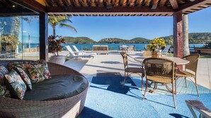 An outdoor seating area with wicker furniture, a table, and chairs, overlooking a scenic coastal view. - Cinematográfica Mansão Pé na Areia  (Búzios)