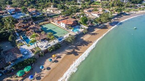 An aerial view of a coastal resort with a tennis court, beach, and ocean. - Cinematográfica Mansão Pé na Areia  (Búzios)