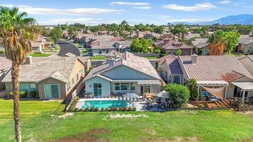 A residential area with houses featuring red-tiled roofs, a swimming pool, and a well-maintained lawn.