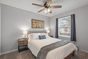 A bedroom with a bed, nightstands, a ceiling fan, a window with curtains, and a wall-mounted artwork. - Tranquil 2BR Apt Mpls - 8075 Apt 3 (Minneapolis)