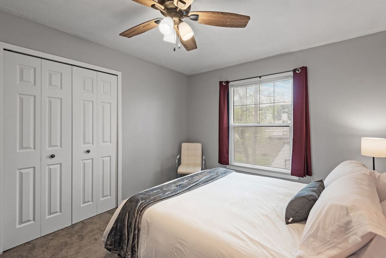 A bedroom with a bed, a ceiling fan, a window with curtains, and a chair.