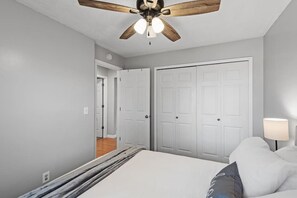 A bedroom with a ceiling fan, a bed, a nightstand, and a door leading to another room.
