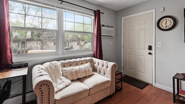 A room with a beige sofa, a window with curtains, a door, and a wall clock. - Tranquil 2BR Apt Mpls - 8075 Apt 3 (Minneapolis)