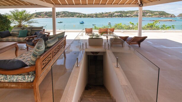 A covered outdoor seating area with wooden furniture and a view of the sea. - Mansão Pé na Areia Ferradura com 4Suítes (Búzios)