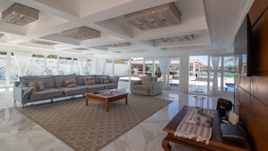A spacious living room with a large gray sofa, a wooden coffee table, and a view of a pool and outdoor area. - Mansão Pé na Areia Ferradura com 4Suítes (Búzios)