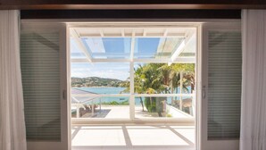 A room with a sliding glass door leading to a balcony with a view of a beach and palm trees. - Mansão Pé na Areia Ferradura com 4Suítes (Búzios)
