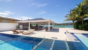 A swimming pool with a sun patio area, lounge chairs, and a covered seating area. - Mansão Pé na Areia Ferradura com 4Suítes (Búzios)
