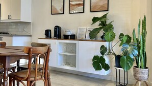 A modern kitchen with white cabinetry, a dining table with wooden chairs, and three framed abstract paintings on the wall.