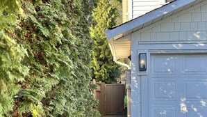 A residential driveway leading to a garage with a white exterior, a wooden fence in the background, and a well-maintained hedge on the left.