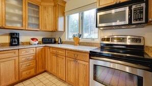 Una cocina con armarios de madera, un microondas, una estufa y una ventana con vista a árboles.