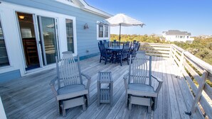 Una terraza de madera con mobiliario exterior, incluyendo sillas y una mesa, y un espacio cubierto con una sombrilla.