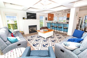 A modern living room with a fireplace, a television, and a kitchen area with bar stools.