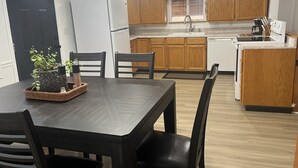 A compact kitchen with wooden cabinets, a white refrigerator, a sink, and a dining area with a table and chairs. - Home away from home (Waldron)