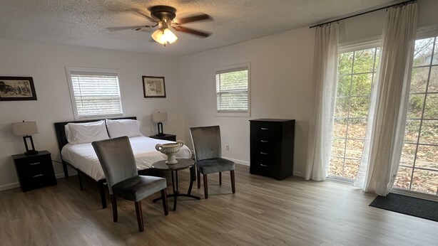 A bedroom with a bed, two chairs, a small table, a nightstand, a dresser, and a ceiling fan. - Home away from home (Waldron)