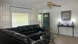 A living room with a black leather sofa, a small round table, a ceiling fan, and a decorative wall piece. - Home away from home (Waldron)