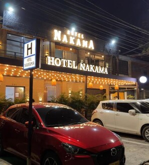 Egy „Hotel Nakama” nevű szálloda, amelyen egy tábla jelzi, hogy szálloda. Két autó parkol az épület előtt.