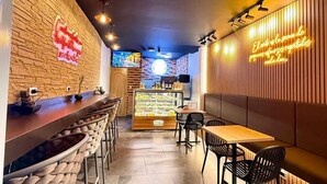 Interior de una cafetería moderna con barra, asientos y una vitrina.