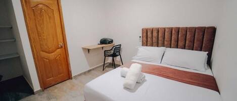 A hotel room with a bed, a desk, a chair, and a wooden door.