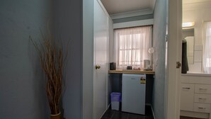 A narrow hallway with a small kitchenette area, a refrigerator, a trash bin, and a window with sheer curtains. - Gundagai Motel (Gundagai)