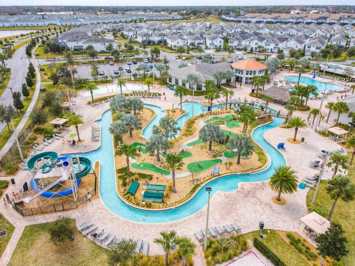 An aerial view of a resort with a large pool area, a water slide, and a golf course.