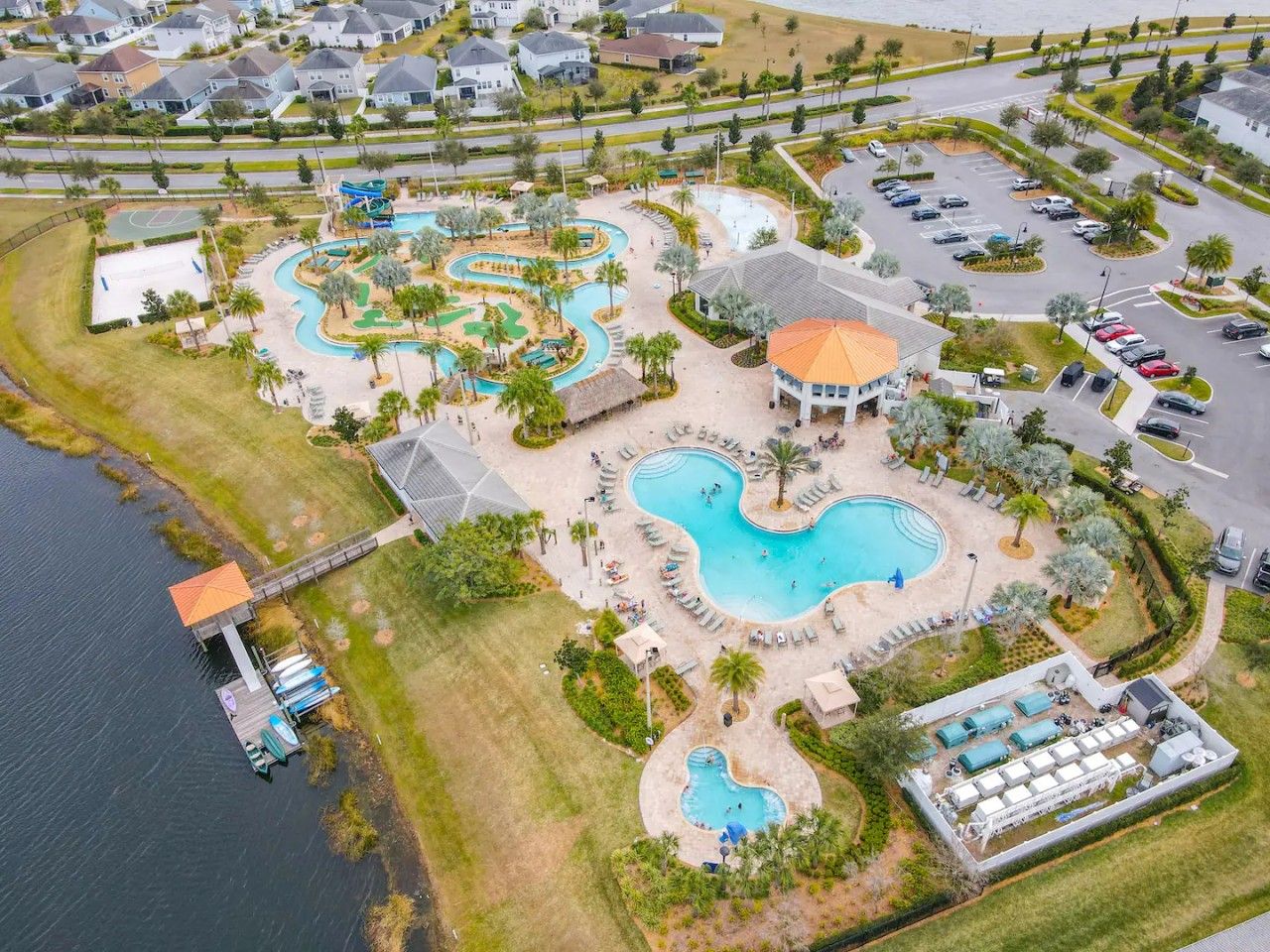 An aerial view of a resort with multiple swimming pools, a dock, and a parking area.