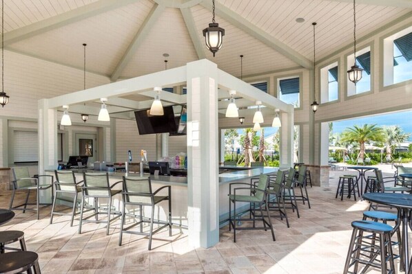 A covered outdoor bar area with seating, a counter, and a TV screen.