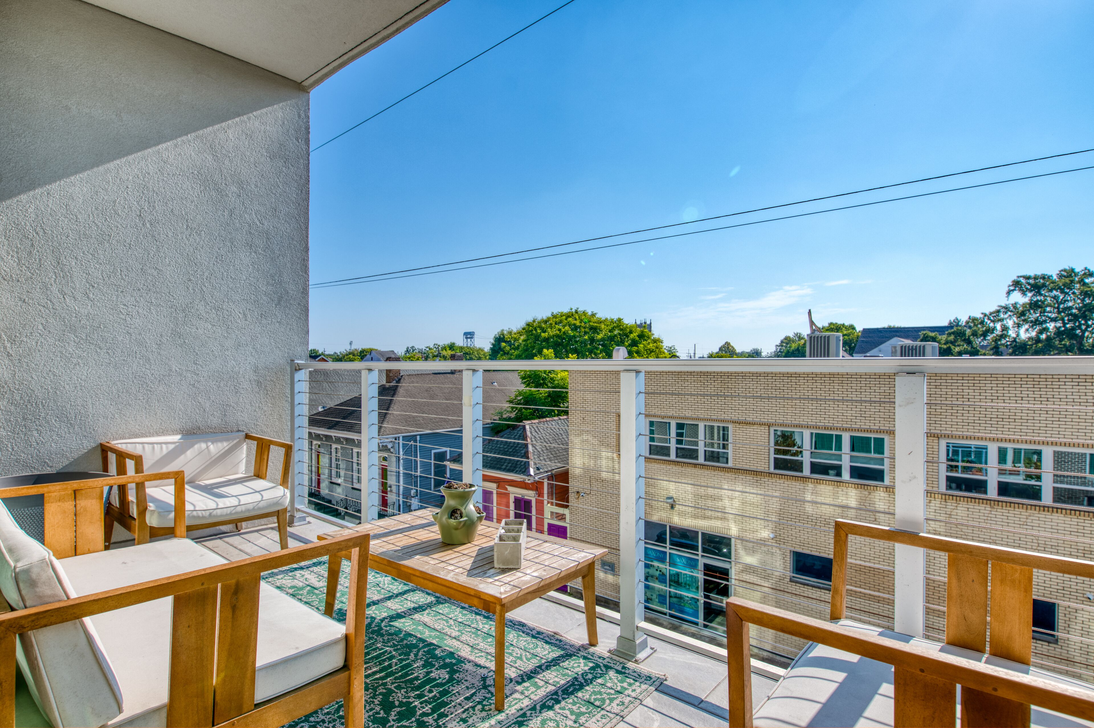 A balcony with outdoor furniture, a view of a brick building, and a clear sky.