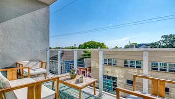 A balcony with outdoor furniture, a view of a brick building, and a clear sky.