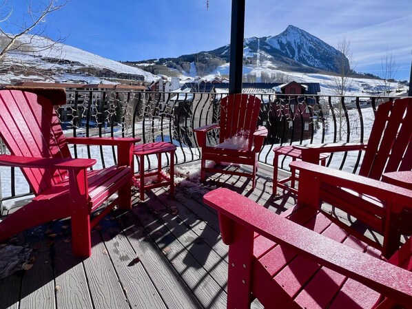 A deck with red Adirondack chairs overlooking a snowy landscape with mountains.