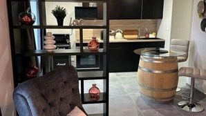 Una sala moderna con un sillón gris oscuro, un barril de madera y una zona de cocina con armarios negros y encimera de madera.