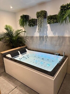 A modern bathroom with a large bathtub, a wall-mounted plant, and a potted palm tree. - Love Room Cocooning Spa (Épinal)