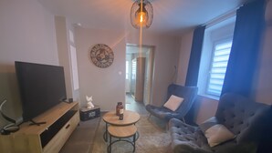 Una sala de estar con un televisor de pantalla plana, una estatua de gato, una mesa redonda, dos sillones y un reloj de pared decorativo.