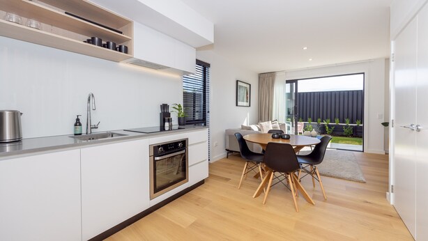 A modern kitchen with white cabinets, a built-in oven, and a dining area with a round table and chairs. - Luxury 3 Bedroom Wanaka Townhouse (Albert Town)
