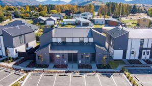 A modern residential complex with multiple detached houses, a central building with a sloped roof, and a parking area. - Luxury 3 Bedroom Wanaka Townhouse (Albert Town)