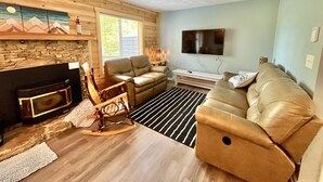 Un salón acogedor con chimenea, sofás de cuero, un sillón mecedor y un televisor de pantalla plana montado en la pared.