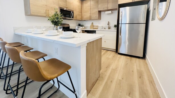 A modern kitchen with a central island, bar stools, stainless steel appliances, and wooden cabinetry. - 4173-Newly renovated stylish home (San Diego)