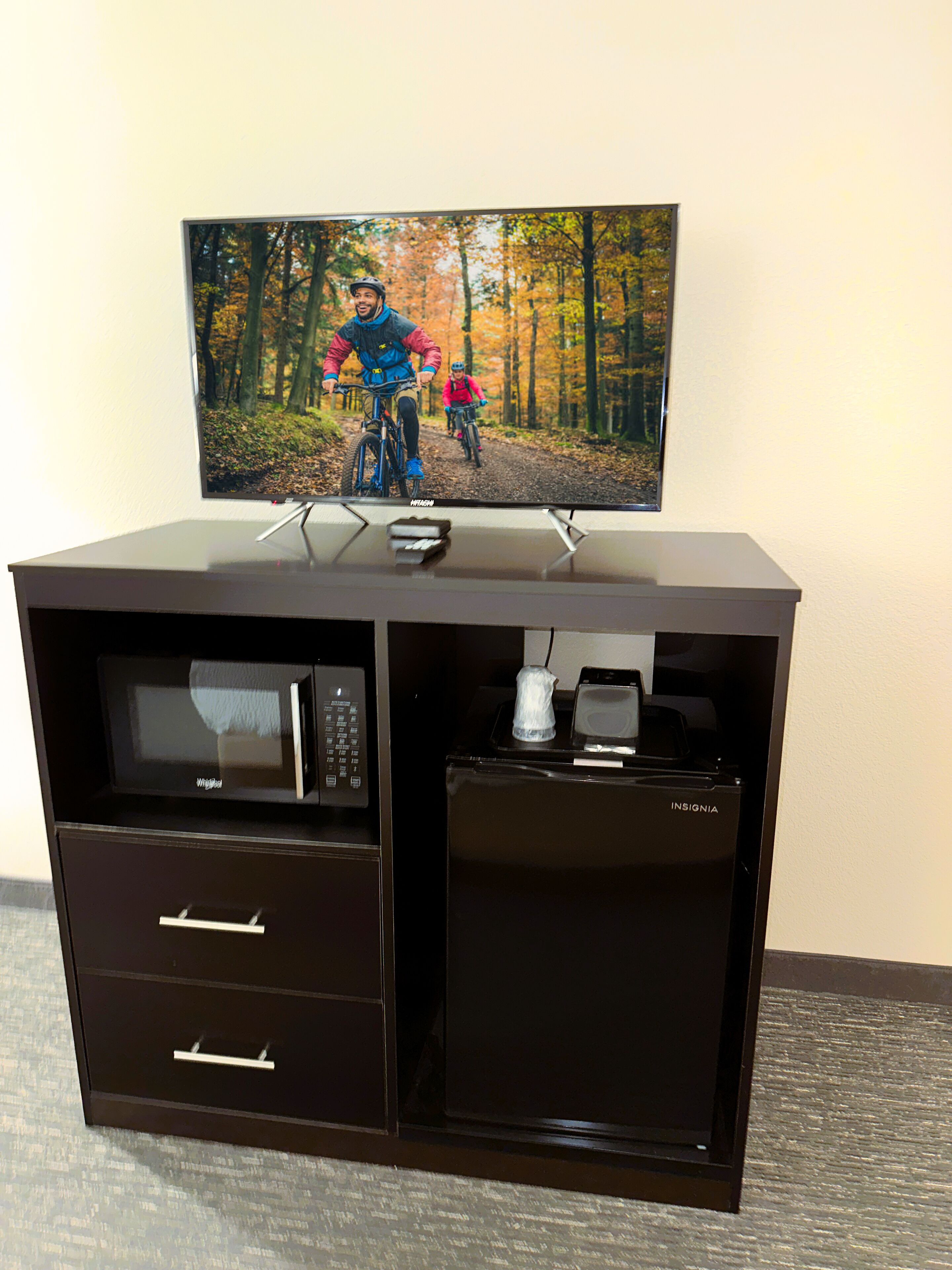 A minibar with a television displaying a mountain biking scene, a microwave, and a coffee maker.