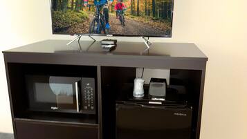 Un minibar con un televisor mostrando una escena de ciclismo de montaña, un microondas y una cafetera.