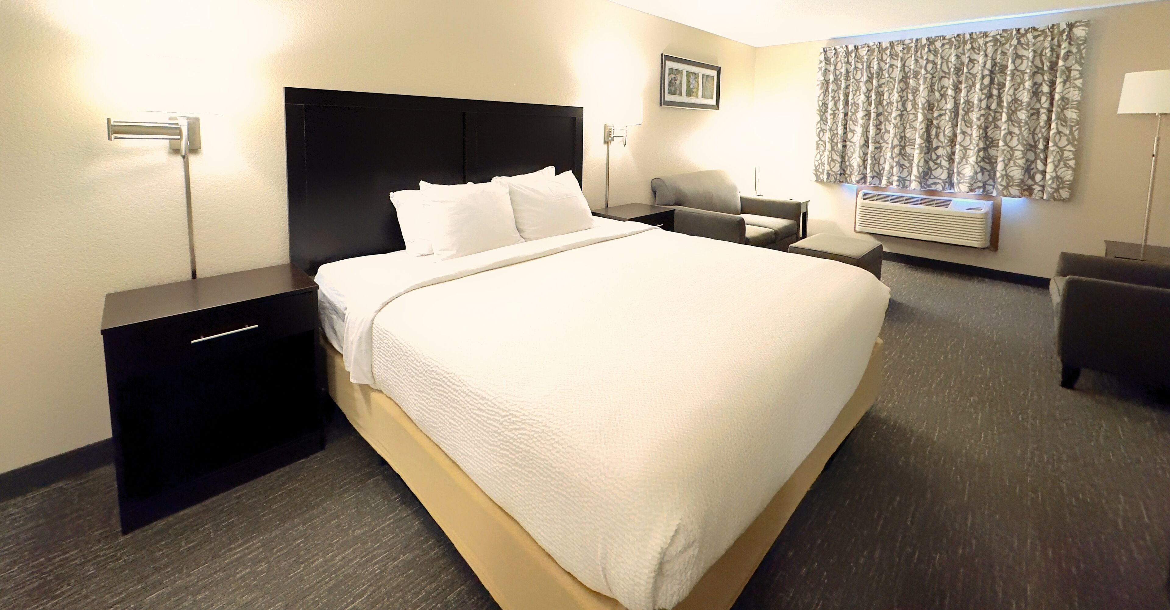 A hotel room with a large bed, a nightstand, a desk, a chair, and a window with curtains.