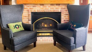 A living room with a brick fireplace, two armchairs with decorative pillows, and a framed map on the wall. - Country Trails Inn & Suites  (Preston)