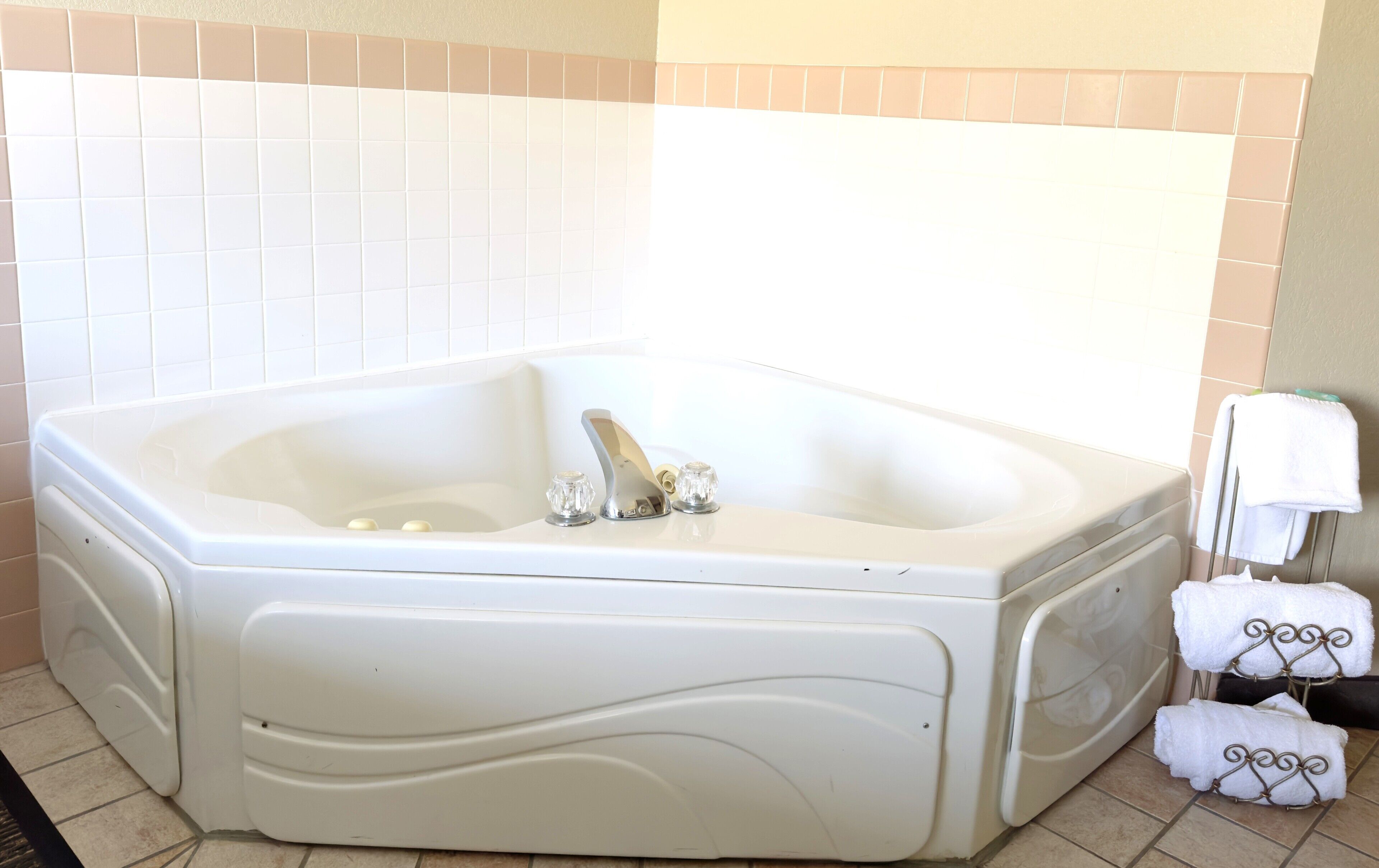 A large, white, freestanding bathtub with a curved design, a single faucet, and two soap dishes. There are two white towels on a metal rack to the right.