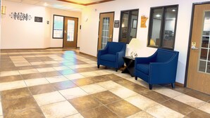 A lobby with a checkered floor, two blue armchairs, a table with a lamp, and a 'WELCOME' sign. - Country Trails Inn & Suites  (Preston)