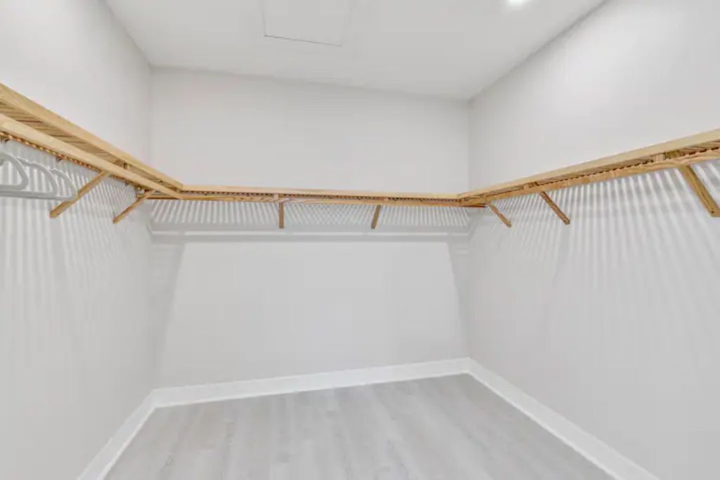 Una stanza con pareti bianche, pavimento in legno e un angolo con scaffali in legno.
