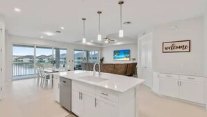 Una cocina moderna con una isla grande, armarios blancos, iluminación colgante y vistas al exterior.