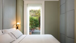 A bedroom with a bed, a nightstand, a lamp, and a view of a garden through an open door. - Mastroianni House with Terrace by Hostalia (Roma)