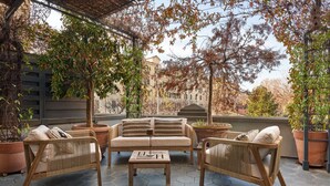 An outdoor patio with a sofa set, two chairs, and a coffee table. There are potted plants and a pergola overhead. - Mastroianni House with Terrace by Hostalia (Roma)